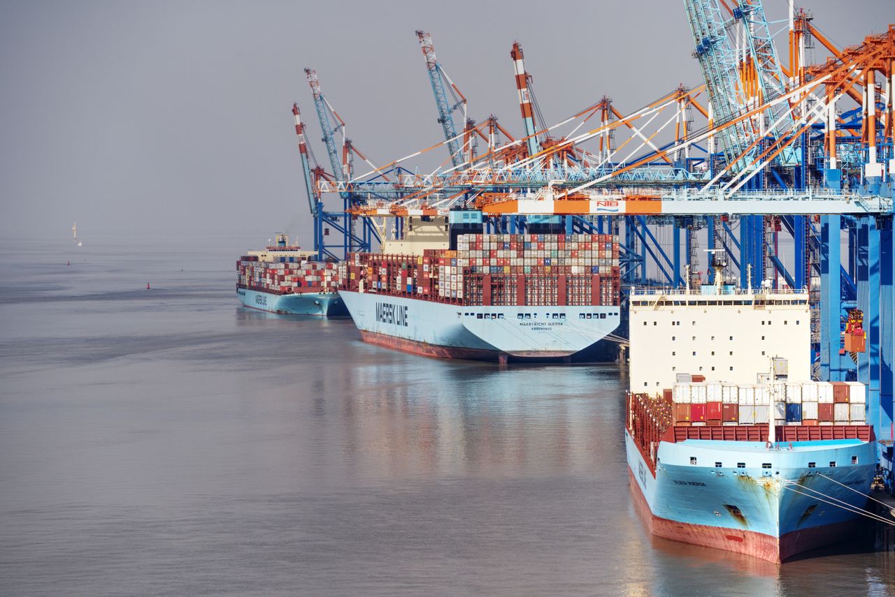 Home Container ships docked at a busy port with vibrant cranes and clear skies.