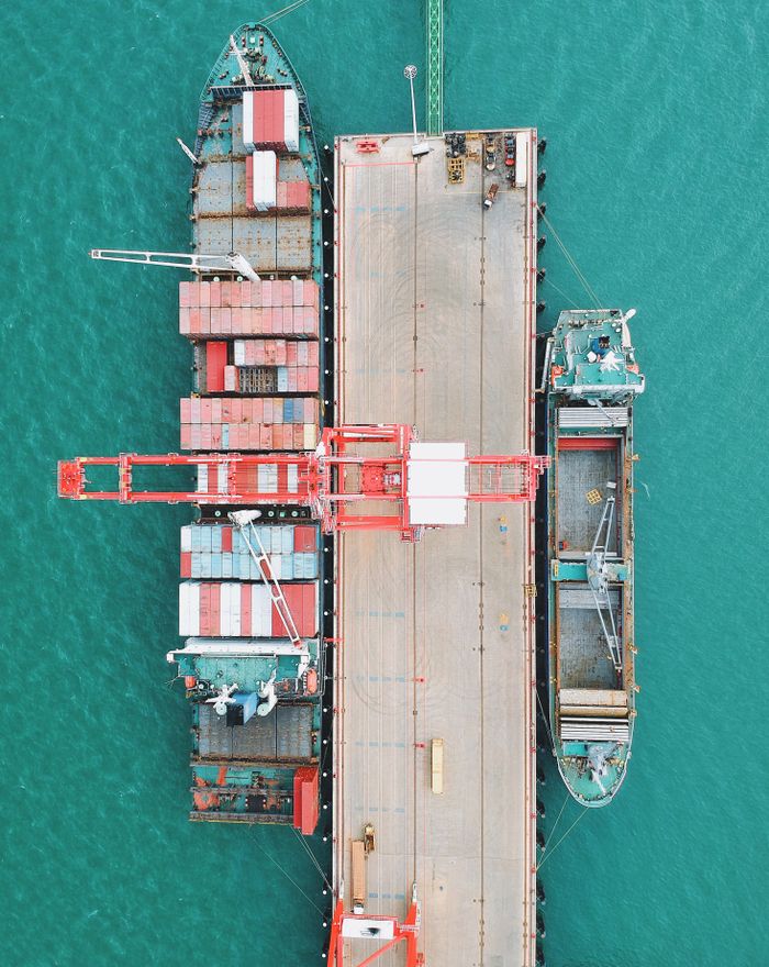 Home Aerial shot of cargo ships docked at a harbor with cranes and containers.